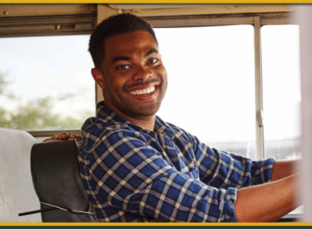 bus driver in plaid shirt smiling while driving school bus