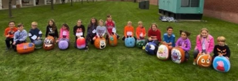 students sitting with their newly decorated pumpkins on the school lawn 