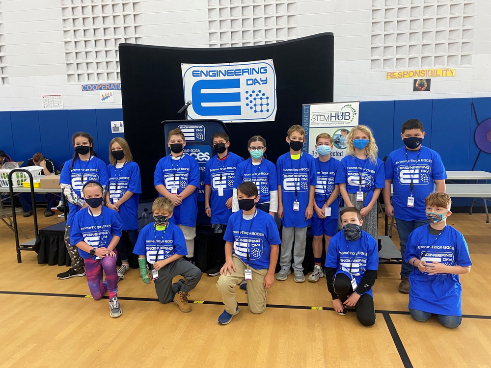 A group of students in blue t-shirts standing at an engineering event