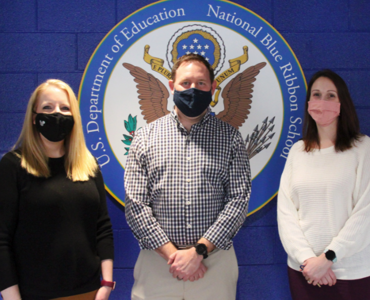 three teachers posing in front of US department of education, National Blue Ribbon School seal on blue wall