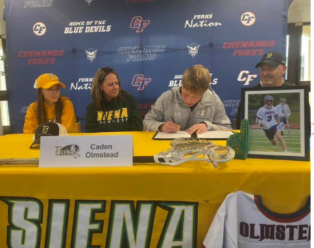 Caden Olmstead signing NLI to play lacross on table with yellow college of siena flag on top