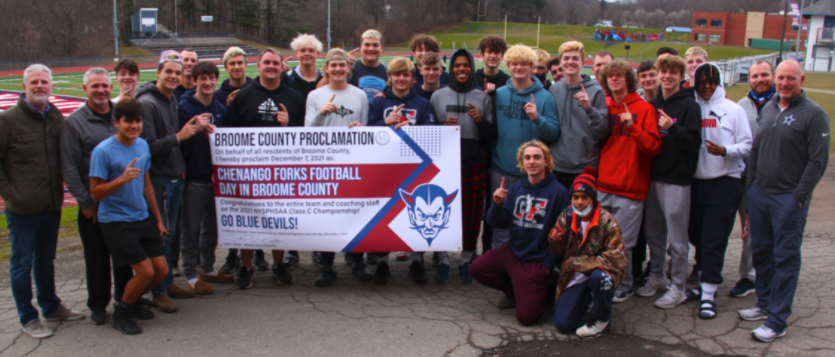 Chenango Forks football team posing with Broome County banner in front of football field