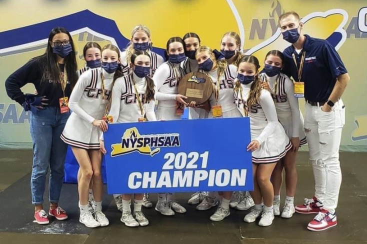 cheerleading team in white uniforms and coaches posing with blue 2021 champion sign